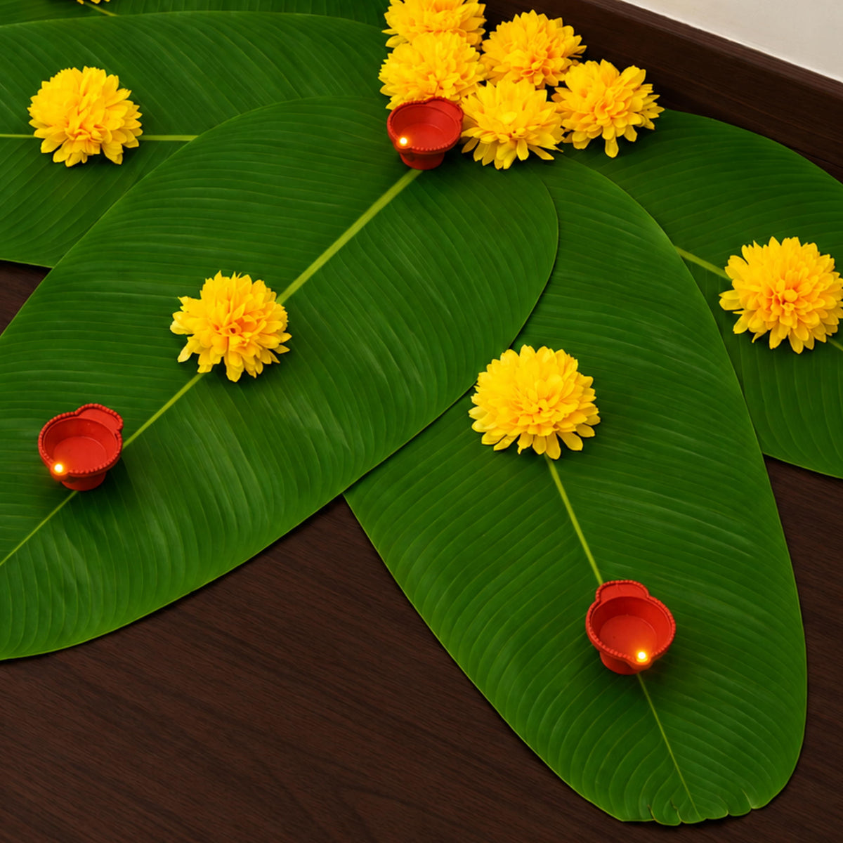 Close view of the banana leaf rangoli showing marigolds and a red LED diya along each leaf