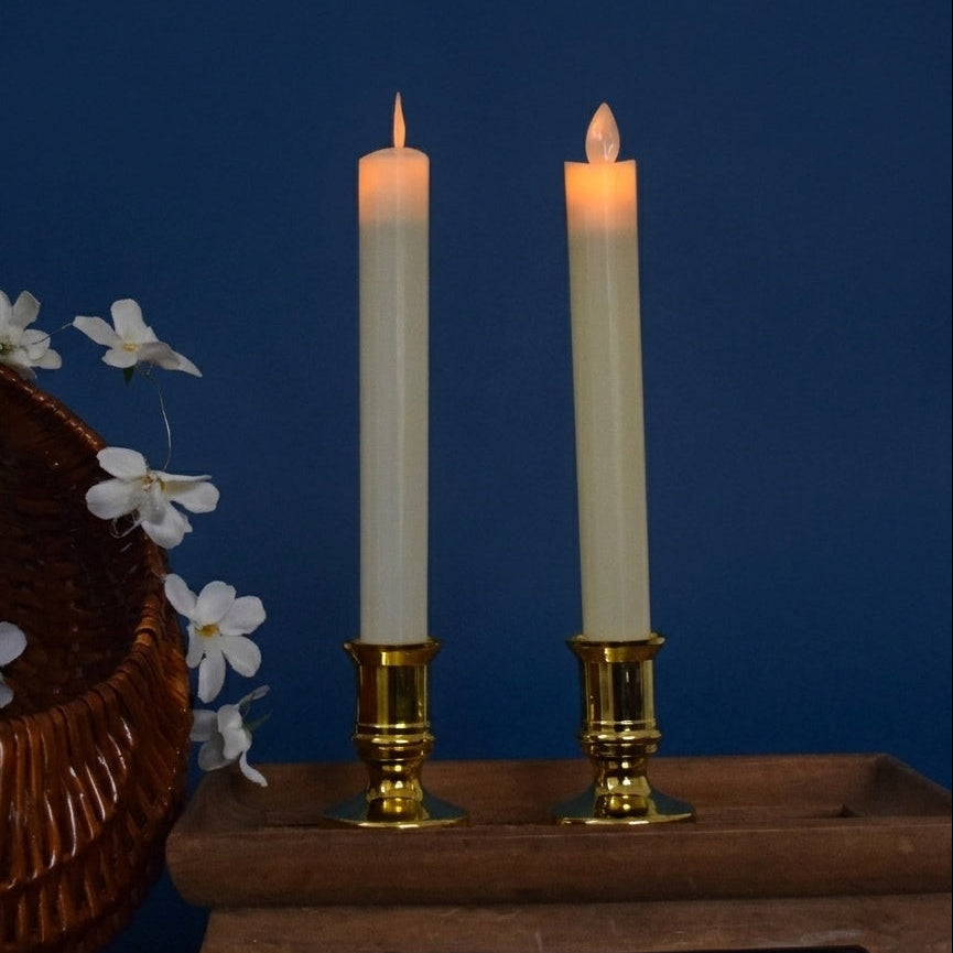 Two lit candles in gold holders with a wicker basket and white flowers on a blue background