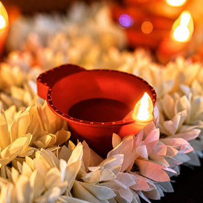 Big flame LED diya glowing among white flowers with more diyas behind