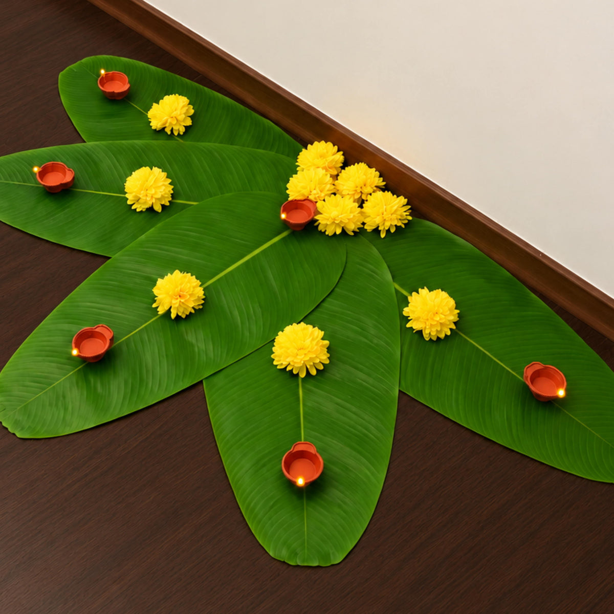 Banana leaf rangoli with yellow marigolds and red LED diyas laid out on a wooden floor