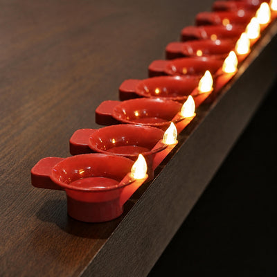 A row of big flame LED diyas lined along a dark wooden ledge