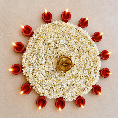 Thirteen big flame LED diyas ringed around a white flower rangoli with a brass lamp at the centre