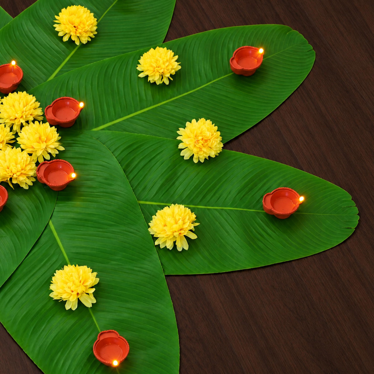 Detail of the banana leaf rangoli with yellow marigolds and lit LED diyas on the leaves