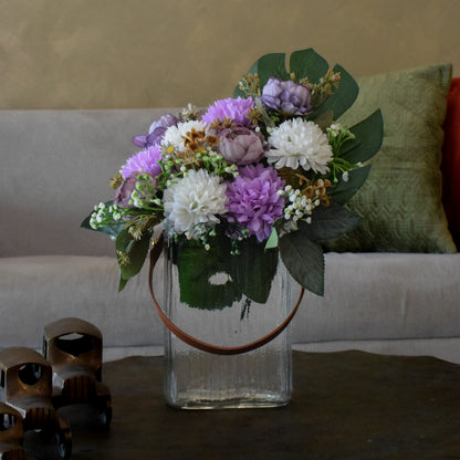 Bouquet of flowers in a glass vase on a table with a couch and decorative pillows in the background.