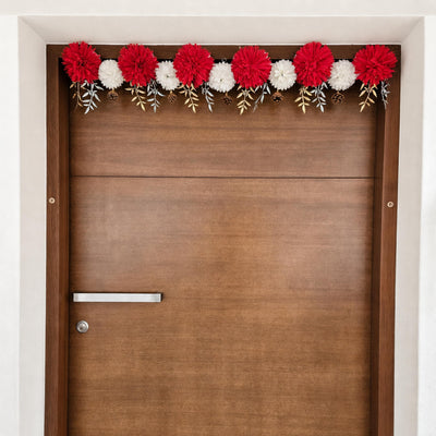 Red and white flower toran with gold leaves across the top of a wood door