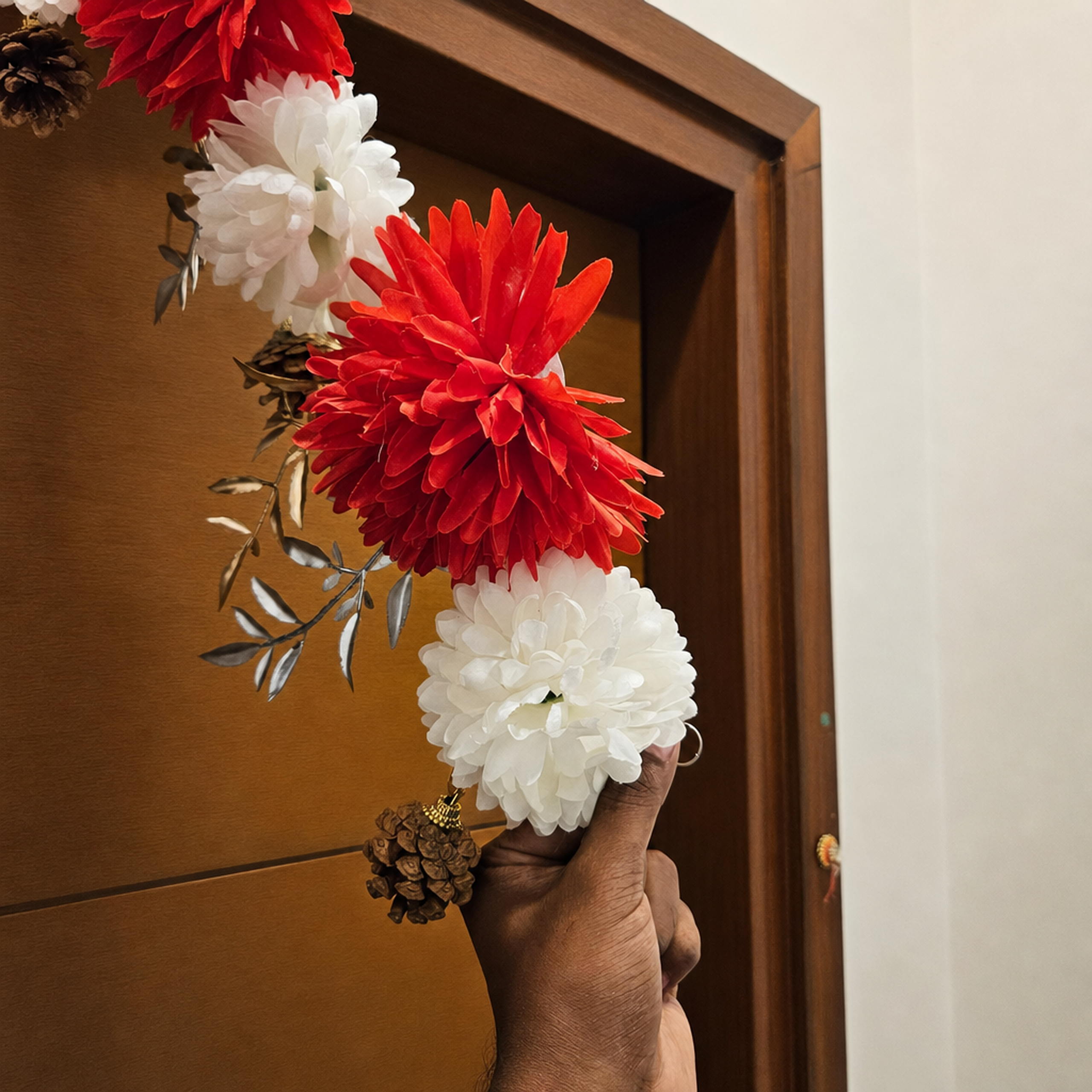 Hand holding the red and white flower toran against a wood door